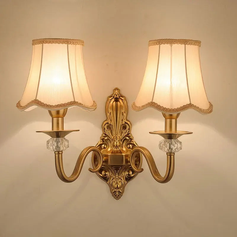 Arandela de parede clássica dourada com duas cúpulas de tecido e cristais decorativos.