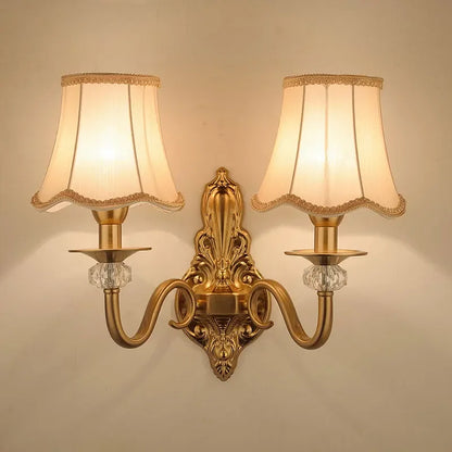 Arandela de parede clássica dourada com duas cúpulas de tecido e cristais decorativos.